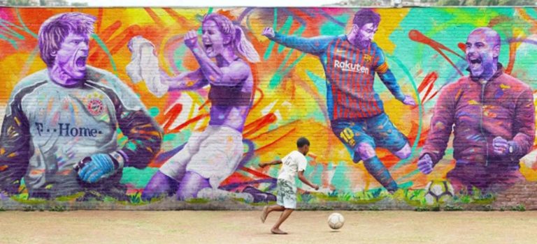 This is Football: mural of football players in Buenos Aires city, a child playing football in front of it